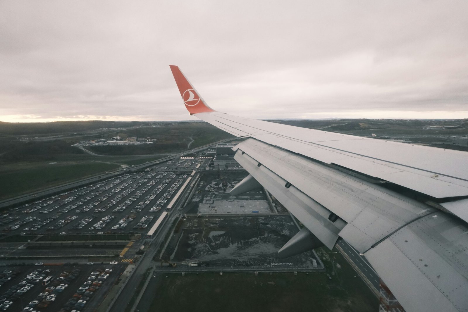 The wing of an airplane flying over a parking lot